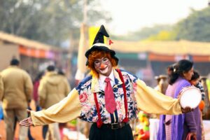 A clown joyfully entertains people at a festival, holding a tambourine while surrounded by vibrant decorations.